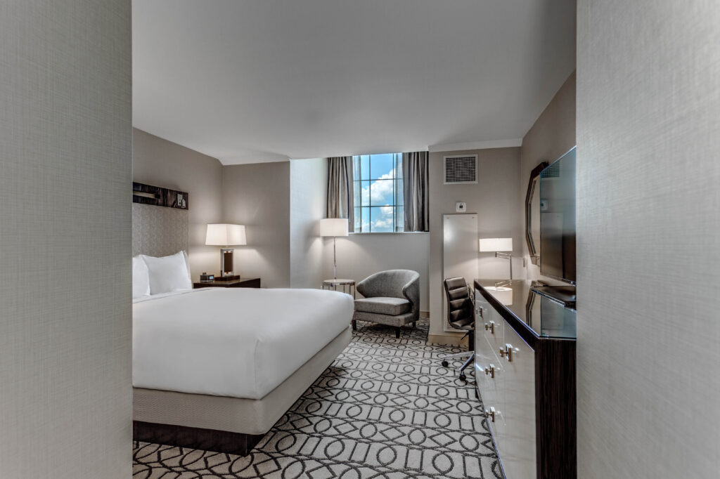 Hotel room with a bed, dresser, natural lighting, and a window.